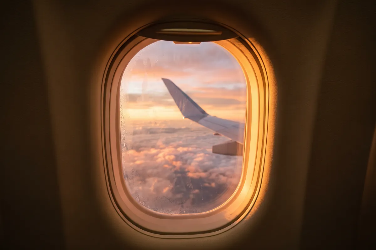 A wingtip above a sea of cloud at sunset, seen through a cabin window